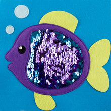 Cargar imagen en el visor de la galería, Una actividad para trabajar con los más chiquitines de casa el desarrollo sensorial e iniciarse en los colores, ya que, al pasar sus manos por el “traje” del pez podrán sentir sus “escamas” y cambiarlo de color. Los brillos de las lentejuelas también atraerán mucho su atención.